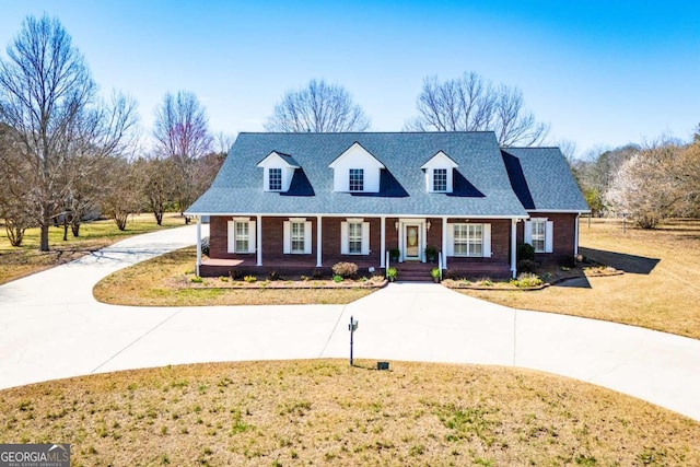 new england style home featuring brick siding, a shingled roof, concrete driveway, and a front yard