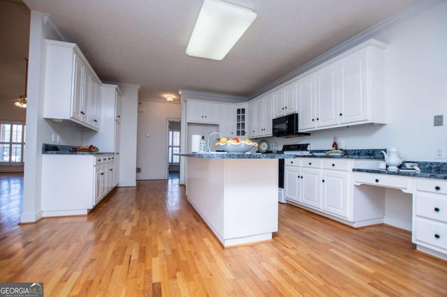 kitchen with black microwave, white cabinetry, light wood-style flooring, and stove