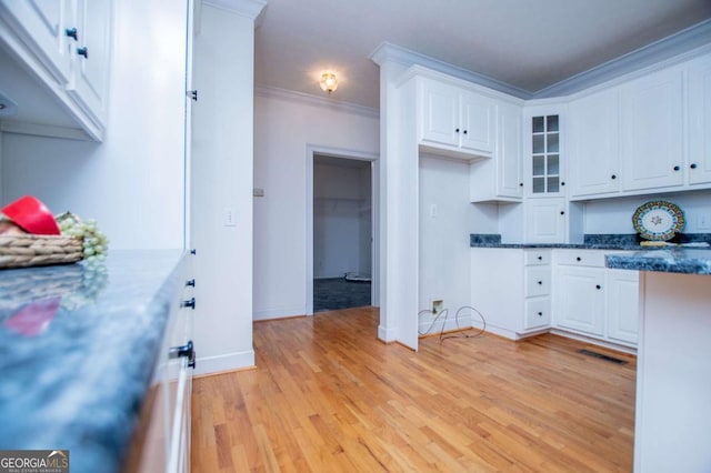 kitchen featuring visible vents, white cabinets, ornamental molding, light wood finished floors, and glass insert cabinets