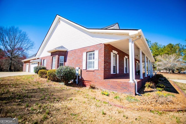 view of property exterior with covered porch, brick siding, driveway, and an attached garage