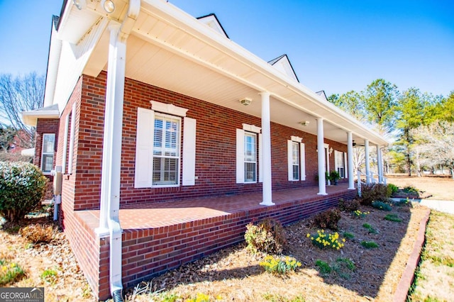 view of side of home featuring covered porch and brick siding