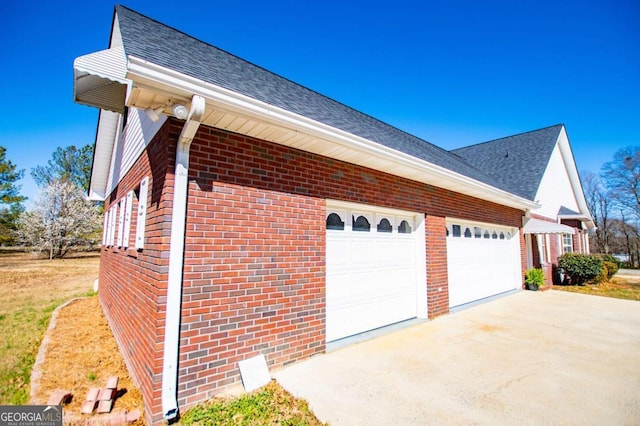 view of side of property featuring brick siding, driveway, and roof with shingles