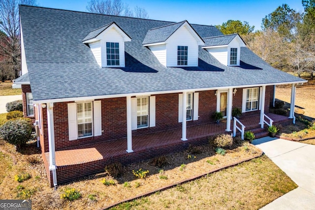 new england style home with covered porch, roof with shingles, and brick siding