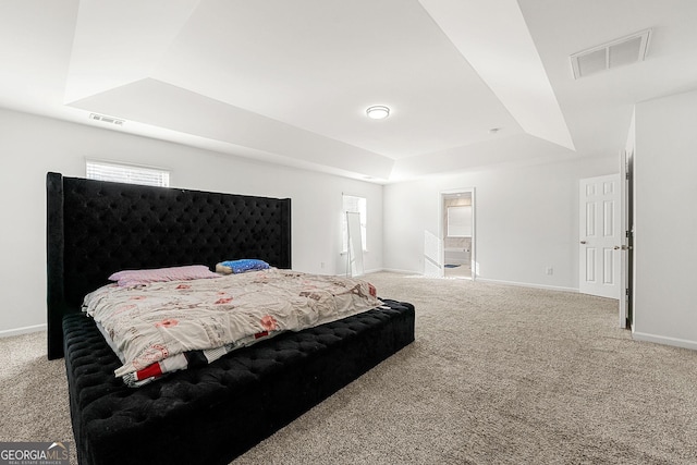 carpeted bedroom with baseboards, visible vents, a raised ceiling, and ensuite bathroom