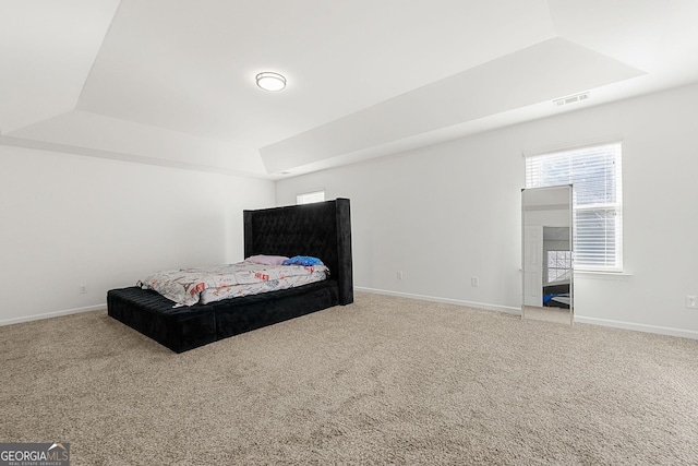 bedroom featuring light carpet, a tray ceiling, multiple windows, and visible vents