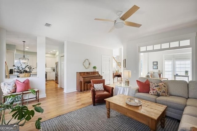 living area featuring visible vents, light wood-style floors, and ceiling fan with notable chandelier