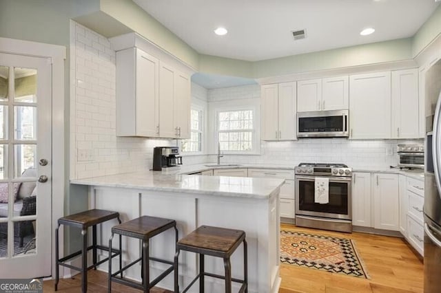 kitchen with light wood finished floors, visible vents, a peninsula, stainless steel appliances, and white cabinetry