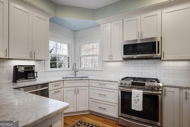 kitchen with light wood-style flooring, a sink, stainless steel appliances, decorative backsplash, and light stone countertops