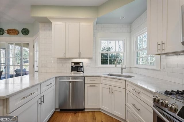 kitchen featuring light wood-style flooring, a peninsula, stainless steel appliances, white cabinetry, and a sink