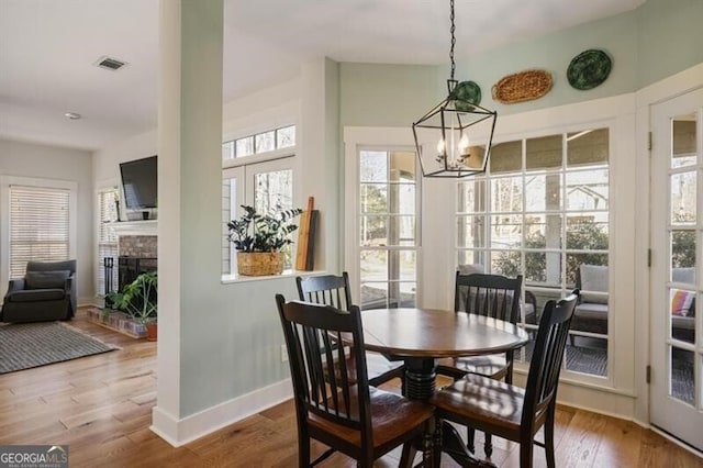 dining room featuring visible vents, wood finished floors, an inviting chandelier, baseboards, and a brick fireplace