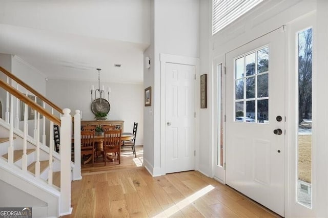 foyer featuring stairway, baseboards, light wood finished floors, and a chandelier