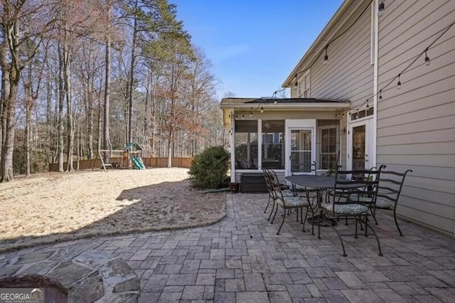 view of patio / terrace featuring a playground, fence, outdoor dining space, and a sunroom