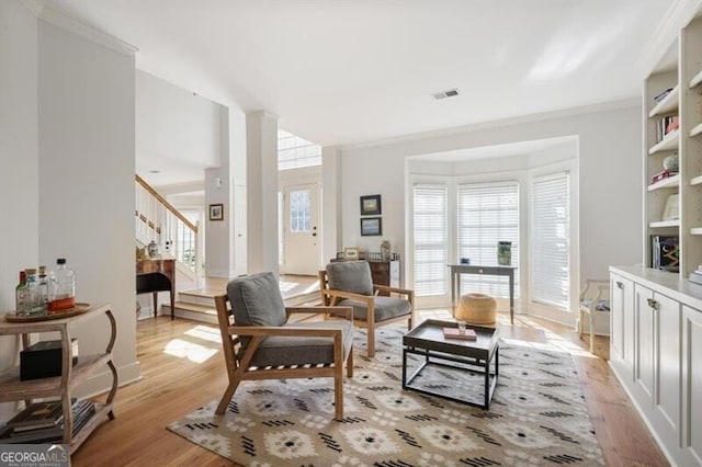 living area with stairs, light wood-style flooring, visible vents, and ornamental molding