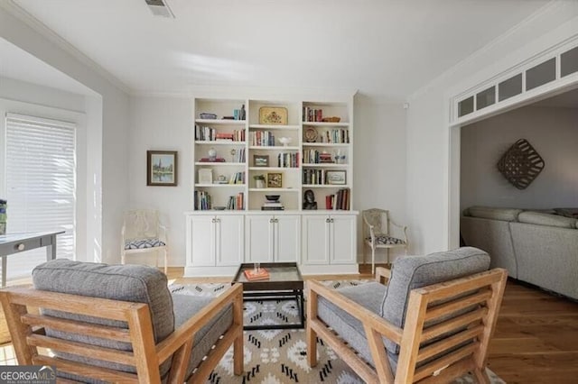 sitting room with visible vents, built in shelves, wood finished floors, and ornamental molding