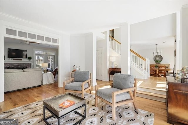 living area featuring light wood-type flooring, a notable chandelier, stairway, a fireplace, and crown molding