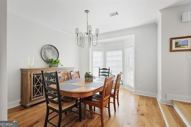 dining room with a notable chandelier, visible vents, light wood finished floors, and ornamental molding