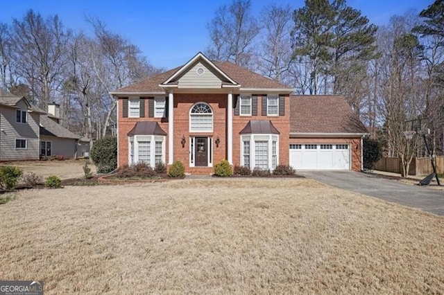 neoclassical home with a front lawn, aphalt driveway, fence, an attached garage, and brick siding