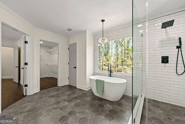 full bath featuring visible vents, a freestanding tub, a shower stall, a walk in closet, and crown molding