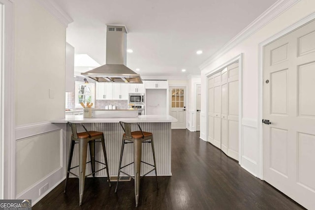 kitchen with a kitchen bar, stainless steel appliances, a peninsula, island range hood, and crown molding