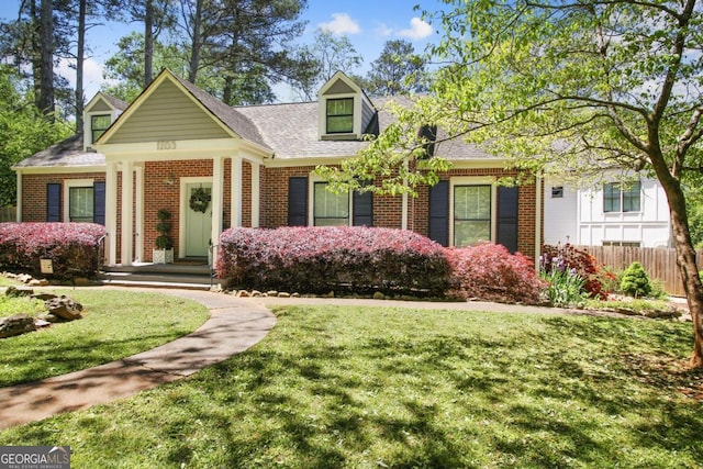 cape cod house featuring roof with shingles, brick siding, a front lawn, and fence