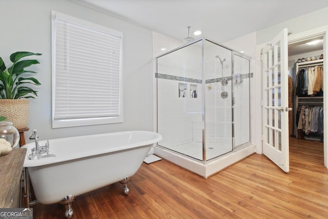 bathroom with a soaking tub, a shower stall, a spacious closet, and wood finished floors