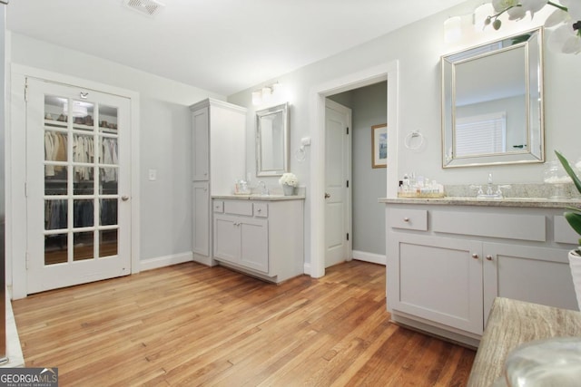 bathroom with a sink, two vanities, wood finished floors, visible vents, and baseboards