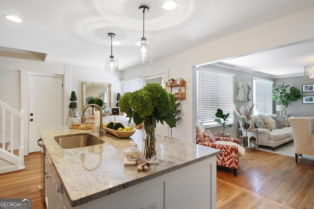 kitchen featuring a sink, light wood-style floors, open floor plan, an island with sink, and pendant lighting