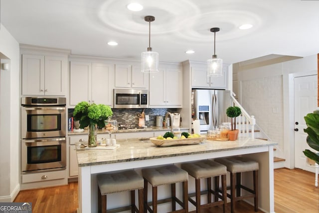 kitchen with a breakfast bar, hanging light fixtures, appliances with stainless steel finishes, light wood finished floors, and tasteful backsplash