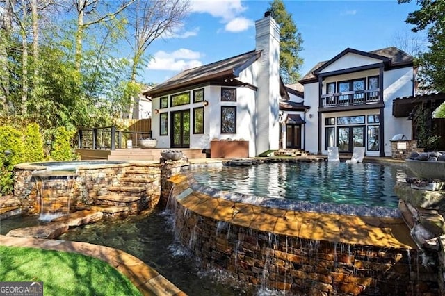 back of property with an in ground hot tub, french doors, a chimney, and stucco siding