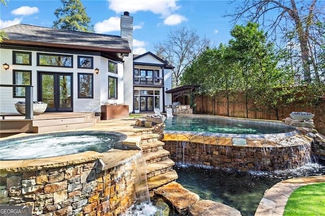 outdoor pool featuring fence, french doors, and an in ground hot tub