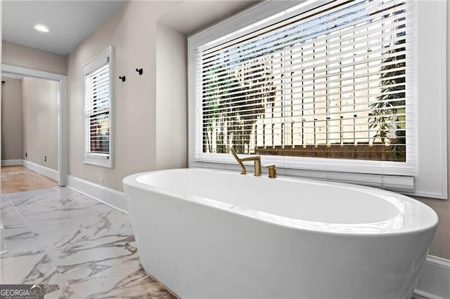 full bathroom featuring marble finish floor, a healthy amount of sunlight, a soaking tub, and baseboards