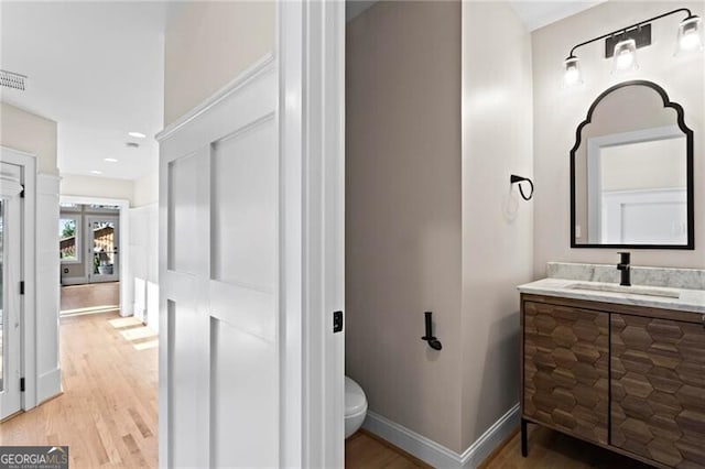 bathroom featuring visible vents, baseboards, toilet, wood finished floors, and vanity