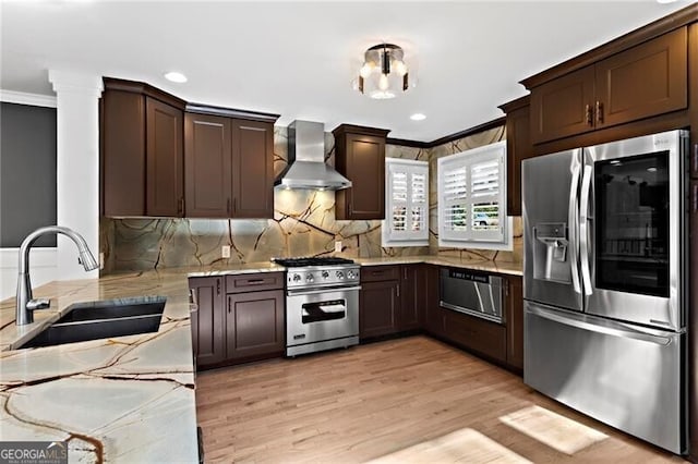 kitchen featuring stainless steel appliances, a sink, a warming drawer, wall chimney exhaust hood, and crown molding