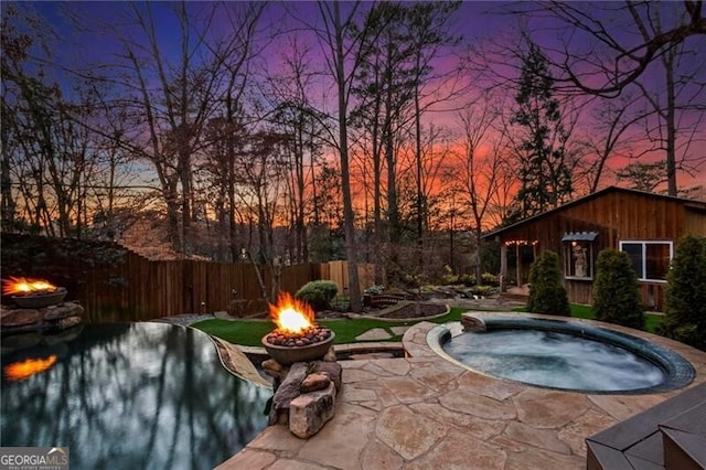 pool at dusk featuring a fire pit, an in ground hot tub, a patio, and fence