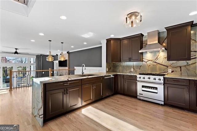 kitchen featuring appliances with stainless steel finishes, a peninsula, dark brown cabinets, wall chimney range hood, and a sink