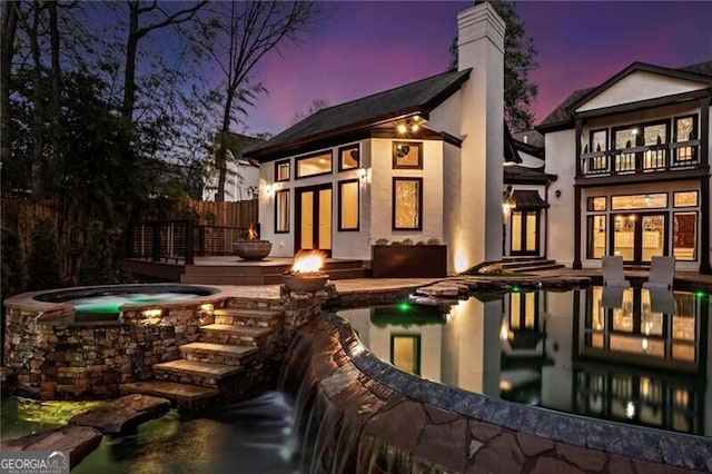 rear view of property with fence, a pool with connected hot tub, french doors, stucco siding, and a chimney