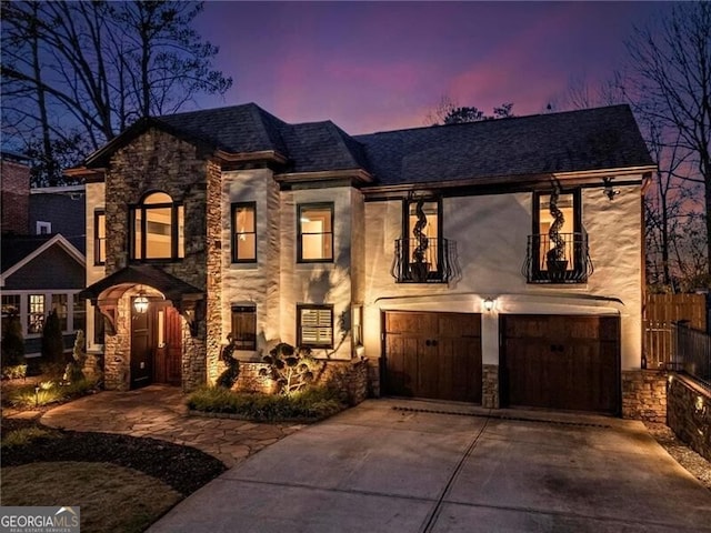 view of front of house with stone siding, concrete driveway, a balcony, and an attached garage