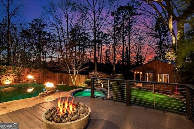 deck at dusk featuring fence, a fire pit, and a fenced in pool