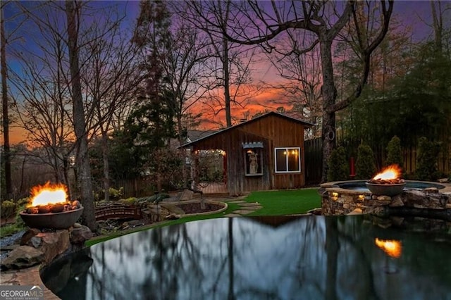 pool at dusk with an outdoor fire pit and a lawn