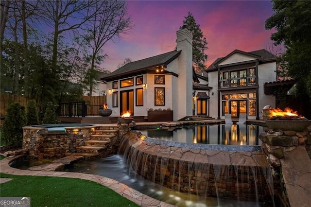 back of house with an in ground hot tub, a chimney, fence, and stucco siding