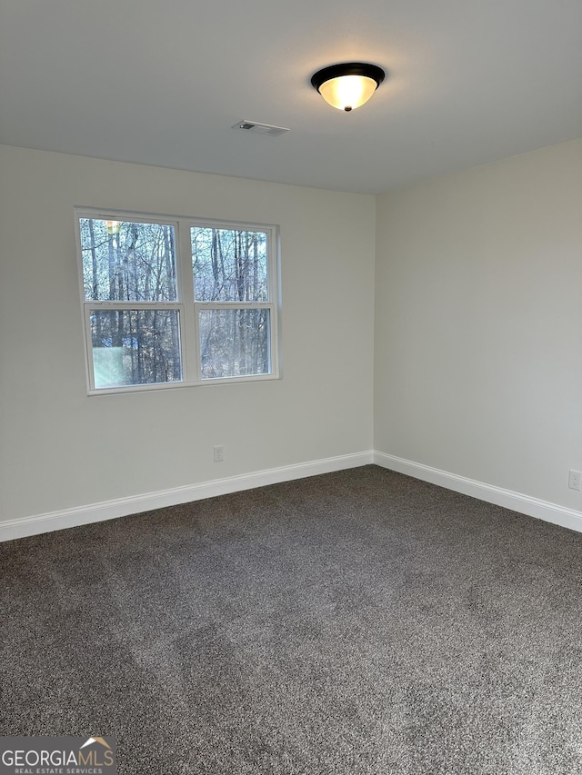 empty room featuring dark colored carpet, visible vents, and baseboards