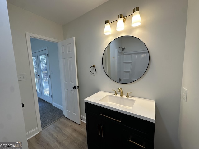 bathroom featuring a shower, french doors, vanity, wood finished floors, and baseboards