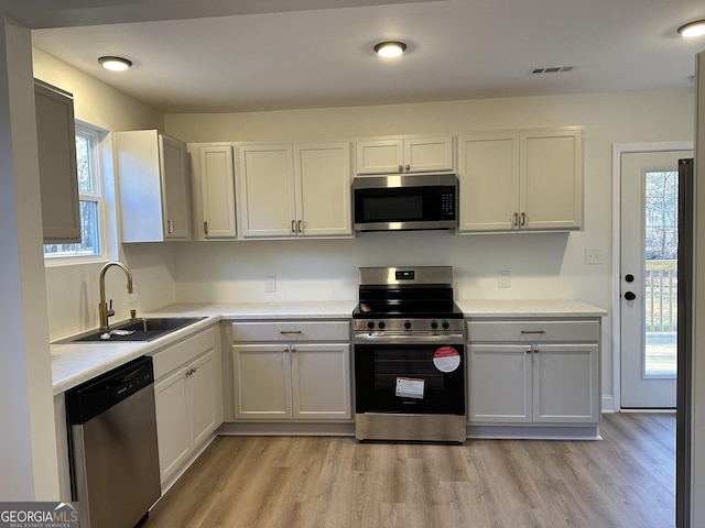 kitchen featuring light countertops, appliances with stainless steel finishes, a sink, and light wood-style floors