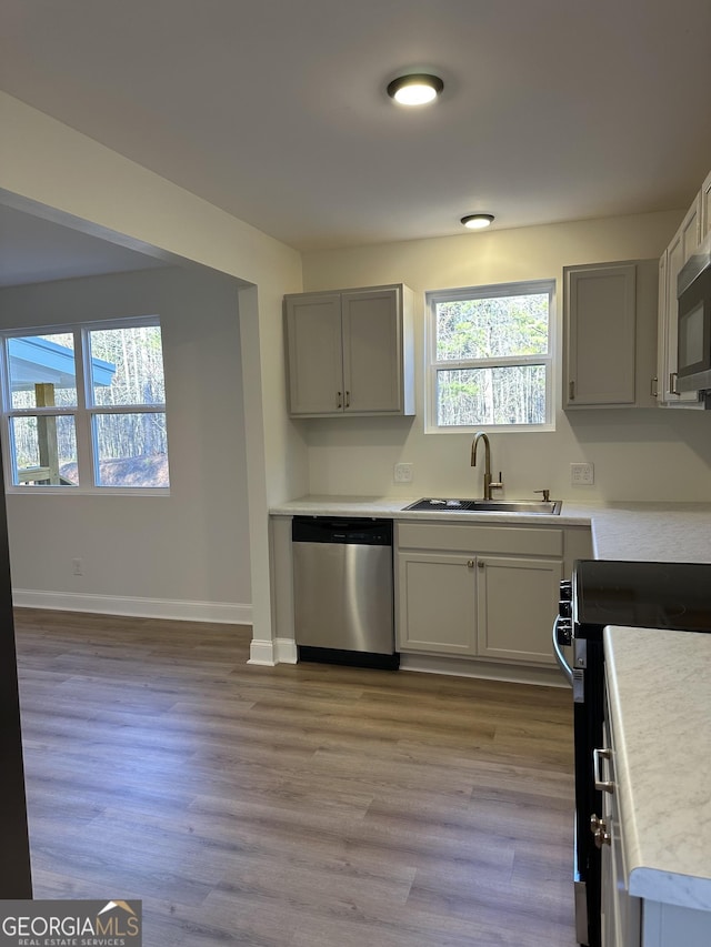 kitchen with stainless steel appliances, a sink, light wood-style floors, light countertops, and plenty of natural light