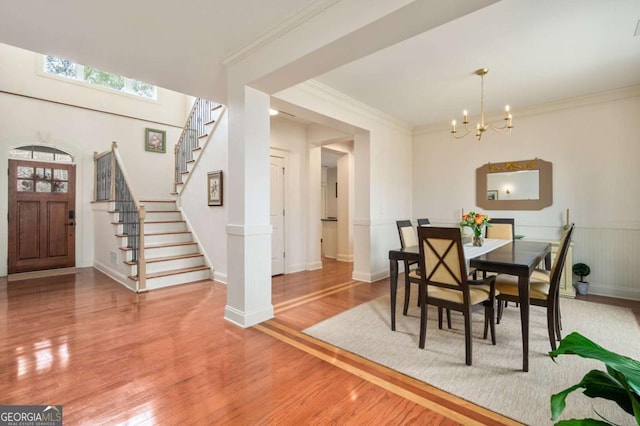 dining room featuring a wainscoted wall, crown molding, stairway, an inviting chandelier, and light wood-type flooring