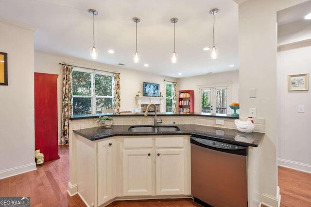 kitchen featuring hanging light fixtures, light wood-style flooring, stainless steel dishwasher, a sink, and dark stone countertops