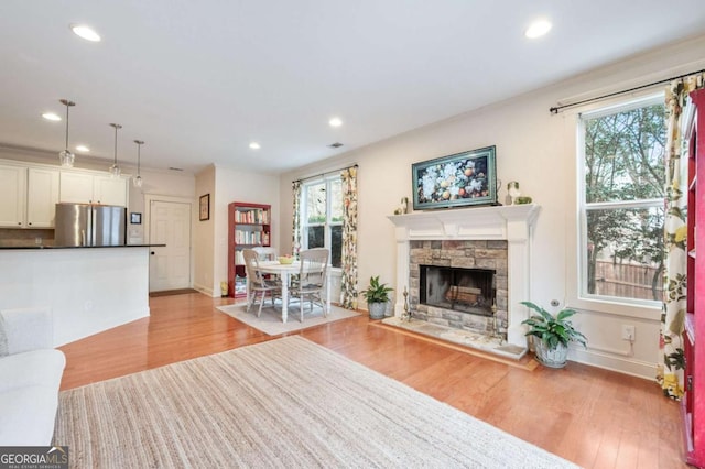 living area with a stone fireplace, recessed lighting, and light wood-style floors