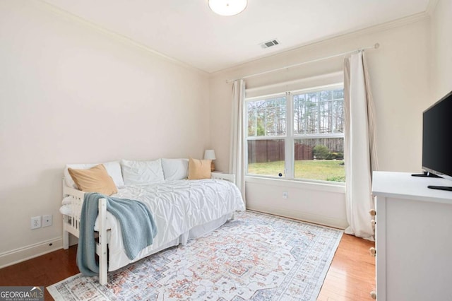 bedroom featuring baseboards, visible vents, crown molding, and wood finished floors