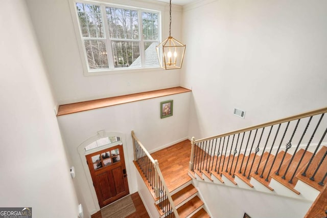 stairway featuring wood finished floors, visible vents, baseboards, and an inviting chandelier