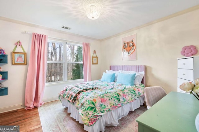 bedroom with visible vents, crown molding, baseboards, and wood finished floors